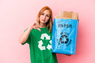 Young caucasian woman recycled paper isolated on pink background showing a dislike gesture, thumbs down. Disagreement concept.