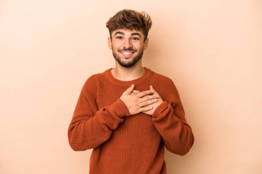 Young arab man isolated on beige background has friendly expression, pressing palm to chest. Love concept.