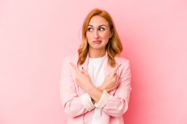 Pembe arka plan noktalarında izole edilmiş genç beyaz kadın iki seçenek arasında seçim yapmaya çalışıyor..