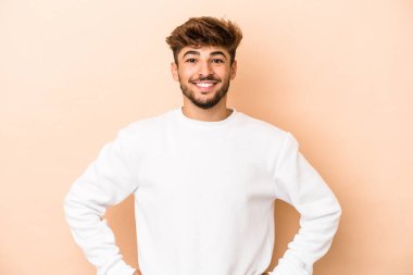 Young arab man isolated on beige background confident keeping hands on hips.