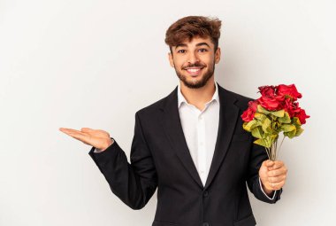 Young mixed race man holding bouquet of roses isolated on white background showing a copy space on a palm and holding another hand on waist.