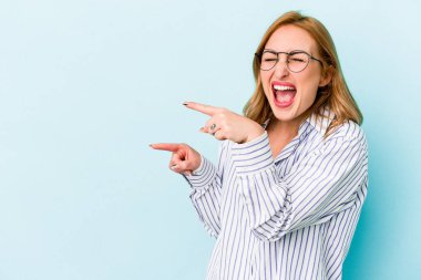 Mavi arka planda izole edilmiş genç beyaz kadın işaret parmağıyla işaret ederek heyecanlanıyor..