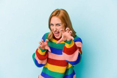 Mavi arka planda izole edilmiş genç beyaz kadın pençelerini kedi taklidi yaparken gösteriyor, agresif bir hareket..