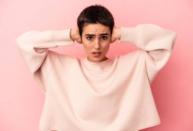 Kafkasyalı genç bir kadın mavi arka planda izole edilmiş kulakları kulaklarıyla kapatıyor çok fazla ses duymamaya çalışıyor..