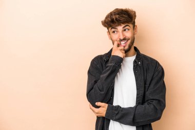 Young arab man isolated on beige background relaxed thinking about something looking at a copy space.