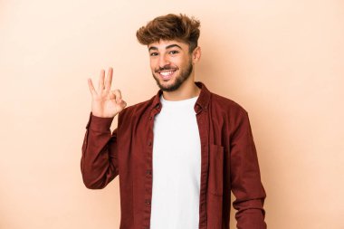 Young arab man isolated on beige background cheerful and confident showing ok gesture.