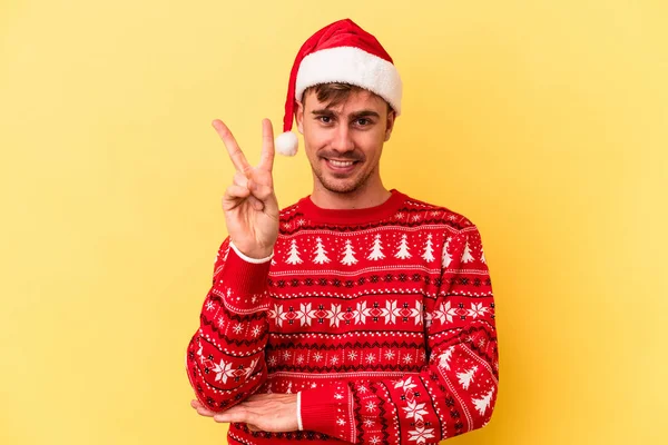若いですCaucasian男祝いますクリスマス絶縁上の黄色の背景ショー番号2とともに指 — ストック写真