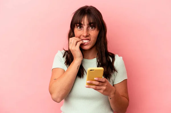 휴대폰을 아르헨티나 여성은 분홍색 배경에 고립되어 손톱을 물어뜯으며 긴장하고 불안해 — 스톡 사진