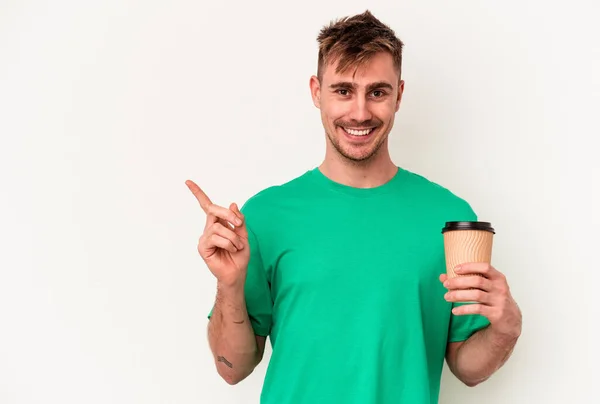 白地の上に孤立したコーヒーを持っている若い白人男性は笑って脇を指差して 空白のスペースで何かを示しています — ストック写真