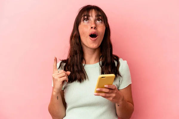 阿根廷年轻女子手持一部粉色背景的手机 上身朝上 张大了嘴 — 图库照片