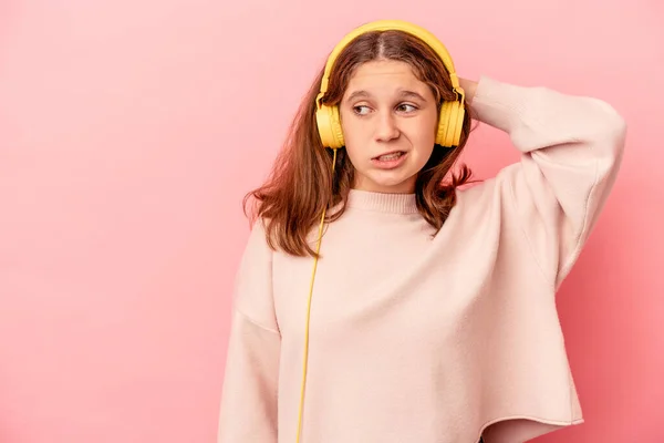 Little caucasian girl listening to music isolated on pink background touching back of head, thinking and making a choice.