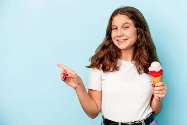 小女孩吃着一个被蓝色背景隔开的冰淇淋 微笑着指着旁边 在空旷的空间里展示着一些东西 — 图库照片