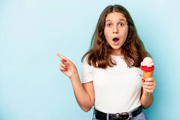 一个白人小女孩正在吃一个用蓝色背景隔开的冰淇淋 指向侧面 — 图库照片