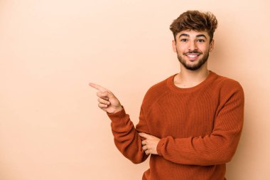 Young arab man isolated on beige background smiling cheerfully pointing with forefinger away.