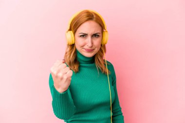 Pembe arka planda izole edilmiş müzik dinleyen beyaz bir kadın kameraya yumruk sallıyor, agresif bir yüz ifadesi var..