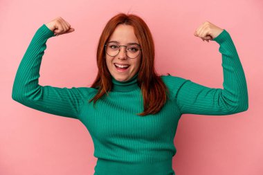 Pembe arka planda izole edilmiş genç beyaz kadın güçlü bir hareket gösteriyor. Kollarıyla, kadınsı gücün sembolü.