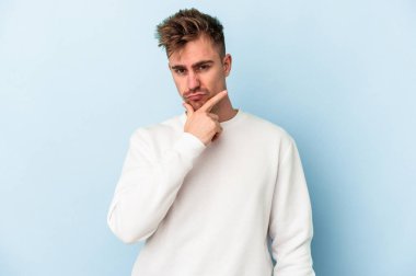 Kafkasyalı genç bir adam mavi arka planda izole edilmiş. Bir strateji planlıyor, bir iş yolu düşünüyor..