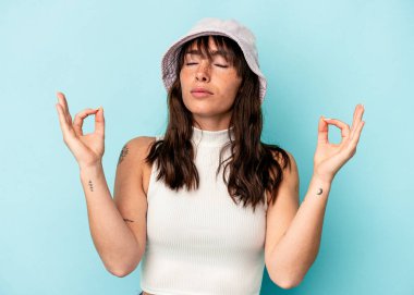 Arjantinli genç kadın mavi arka planda izole edilmiş yoğun bir günün ardından rahatlıyor, yoga yapıyor..
