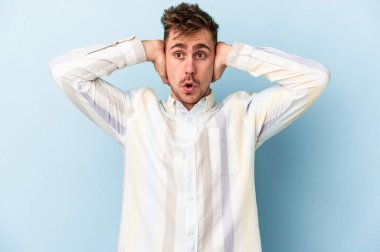 Kafkasyalı genç adam mavi arka planda izole edilmiş kulakları kulaklarıyla kapatıyor çok fazla ses duymamaya çalışıyor..