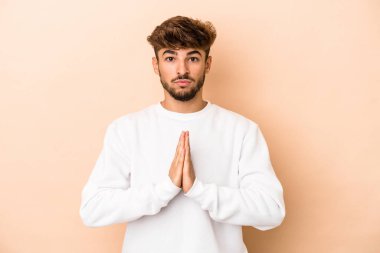 Young arab man isolated on beige background praying, showing devotion, religious person looking for divine inspiration.