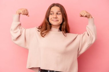 Pembe arka planda izole edilmiş küçük beyaz kız kollarıyla güçlü bir hareket gösteriyor, kadınsı gücün sembolü.
