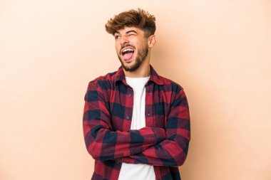 Young arab man isolated on beige background funny and friendly sticking out tongue.