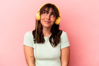 Arjantinli genç bir kadın pembe arka planda izole edilmiş müzik dinliyor. Amaçlarına ve amaçlarına ulaşma hayali kuruyor.