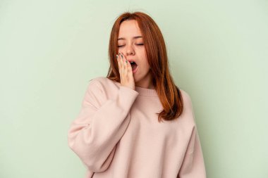 Yeşil arka planda izole edilmiş genç beyaz kadın esniyor. Ağzı eliyle kapatan yorgun bir jest gösteriyor..