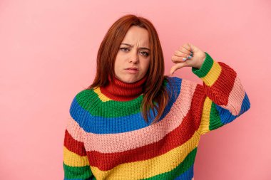 Pembe arka planda izole edilmiş genç beyaz kadın baş parmağını aşağı gösteriyor ve hoşlanmadığını ifade ediyor..