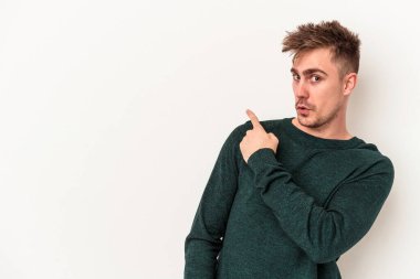Beyaz arka planda izole edilmiş genç beyaz bir adam gülümsüyor ve boş alanda bir şeyler gösteriyor..