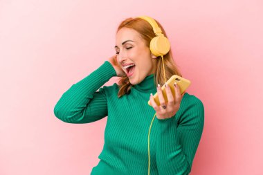 Pembe arka planda izole edilmiş müzik dinleyen beyaz bir kadın.