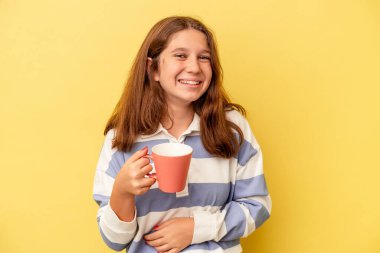 Sarı arka planda pembe kupa tutan küçük beyaz kız gülüyor ve eğleniyor..