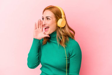 Pembe arka planda izole edilmiş müzik dinleyen beyaz bir kadın bağırıyor ve avuç içi kadar açık bir ağız tutuyor..