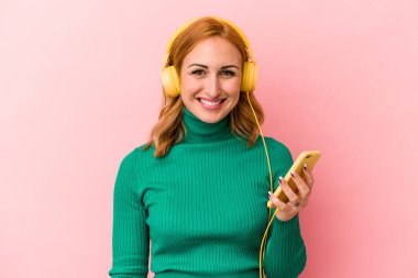 Pembe arka planda izole edilmiş müzik dinleyen beyaz bir kadın.