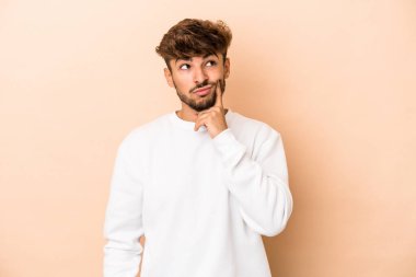 Genç Arap adam bej arka planda izole edilmiş. Bir strateji planlıyor, bir iş yolu düşünüyor..