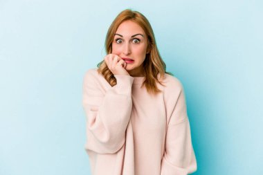 Mavi arka planda izole edilmiş, tırnak yiyen, gergin ve endişeli bir beyaz kadın..