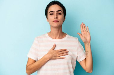 Beyaz bir kadın mavi arka planda izole edilmiş yemin ediyor, elini göğsüne koyuyor..