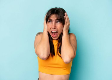 Arjantinli genç bir kadın, mavi arka planda izole edilmiş kulaklarını elleriyle kapatarak yüksek sesle ses duymamaya çalışıyor..