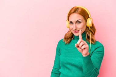 Pembe arka planda müzik dinleyen beyaz bir kadın bir numarayı parmağıyla gösteriyor..