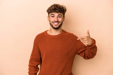 Young arab man isolated on beige background person pointing by hand to a shirt copy space, proud and confident