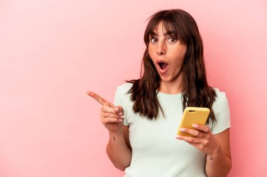 Arjantinli genç bir kadın cep telefonu tutuyor. Pembe arka planda izole edilmiş. Yan tarafı işaret ediyor.