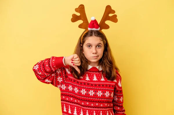 黄色の背景に隔離されたクリスマスのトナカイの帽子をかぶっている小さな白人の女の子は 嫌いなジェスチャー 親指を下に示しています 意見の相違 — ストック写真