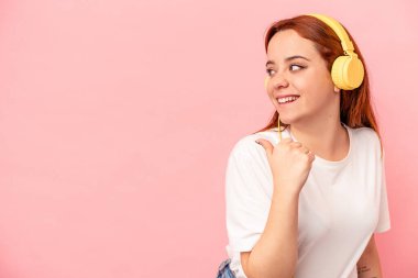 Pembe arka planda müzik dinleyen beyaz bir kadın. Baş parmak uzakta, gülüyor ve kaygısız..