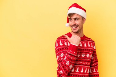 Kafkasyalı genç adam, sarı arka planda izole edilmiş bir şekilde Noel 'i kutluyor. Baş parmak uzakta, gülerek ve kaygısızca..