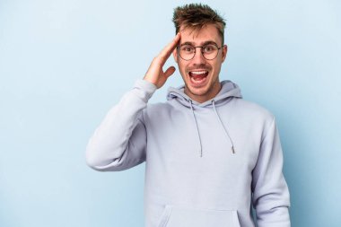 Mavi arka planda izole edilmiş genç beyaz adam yüksek sesle bağırıyor, gözleri açık ve elleri gergin tutuyor..