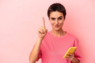 Elinde cep telefonu olan beyaz bir kadın pembe arka planda izole edilmiş. Bir numarayı parmağıyla gösteriyor..