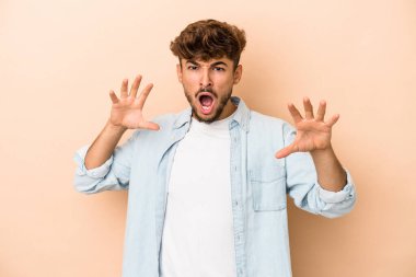 Young arab man isolated on beige background showing claws imitating a cat, aggressive gesture.
