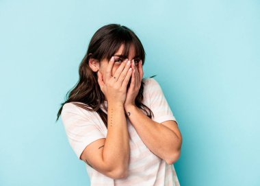 Arjantinli genç bir kadın mavi arka planda izole edilmiş. Kameraya parmaklarıyla göz kırpıyor. Yüzünü kapatmaktan utanıyor..