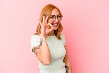 Genç beyaz kadın pembe arka planda izole edilmiş neşeli ve kendinden emin, iyi bir jest yapıyor..