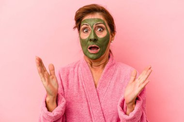 Middle age caucasian woman wearing a facial mask isolated on pink background surprised and shocked.